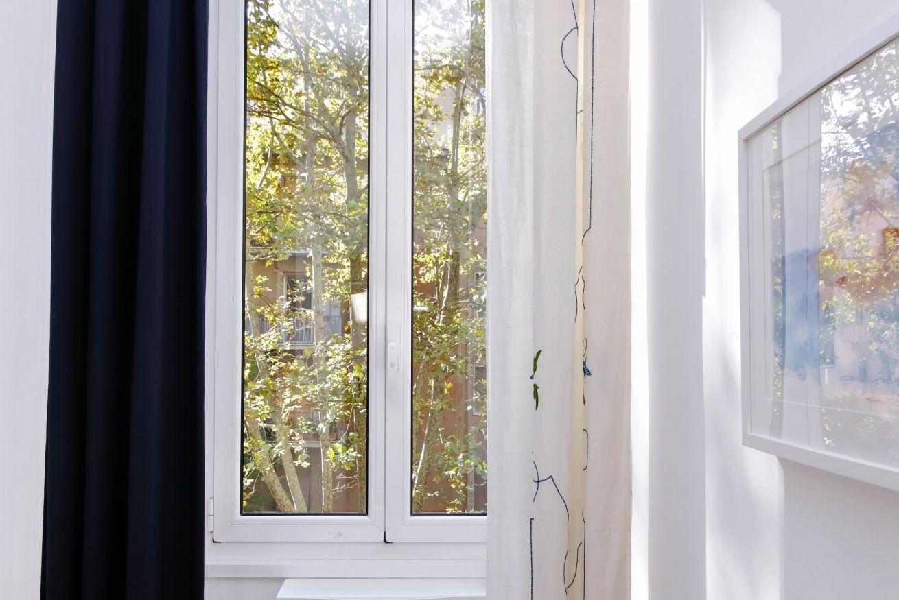 A room with a large window, a white wall, and a black curtain.