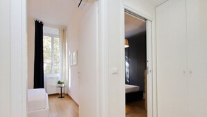A narrow hallway with a white door on the right, a white sofa on the left, and a small table with a plant. - Lovely Rhome  apartment near Vatican (ROMA)