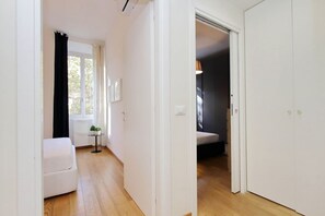 A narrow hallway with a white door on the right, a white sofa on the left, and a small table with a plant. - Lovely Rhome  apartment near Vatican (ROMA)