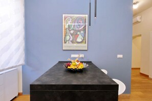 Ein modernes Interieur mit einem schwarzen Tisch, einer Obstschale und einem farbenfrohen, abstrakten Gemälde an der Wand.