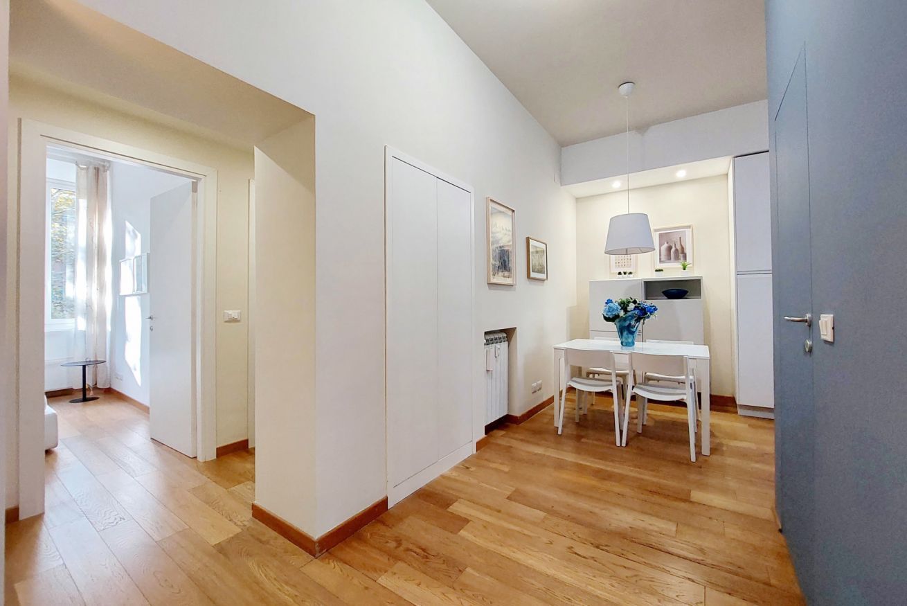 A modern kitchen with white cabinets, a dining table with chairs, and a vase of flowers.