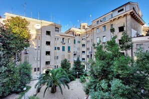 A courtyard with a palm tree and various shrubs, surrounded by multi-story buildings with balconies and air conditioning units. - Lovely Rhome  apartment near Vatican (ROMA)