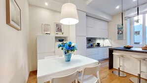 A modern kitchen with white cabinets, a white dining table with four chairs, a vase of flowers, and a bar area with stools. - Lovely Rhome  apartment near Vatican (ROMA)