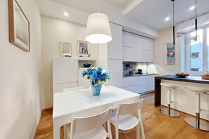 A modern kitchen with white cabinets, a white dining table with four chairs, a vase of flowers, and a bar area with stools. - Lovely Rhome  apartment near Vatican (ROMA)