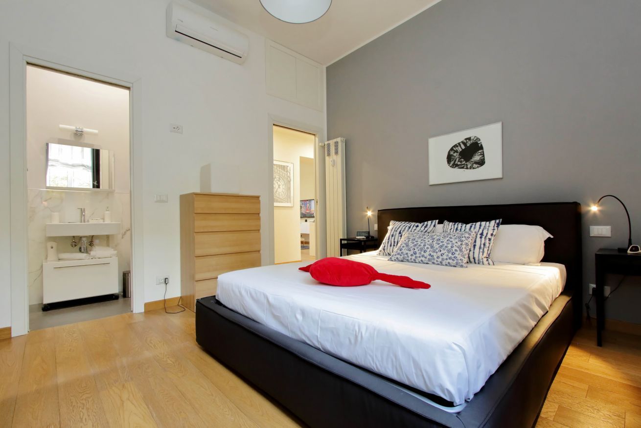 A modern bedroom with a large bed, a bedside table, a nightstand, and a wall-mounted artwork.