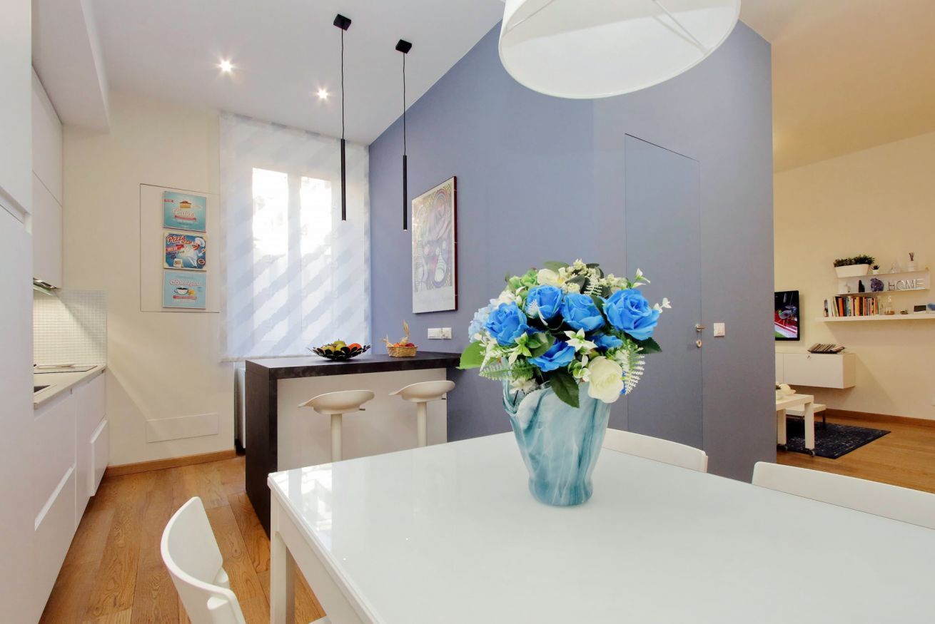 A modern kitchen with white cabinets, a dining table with chairs, and a vase of flowers on the table.