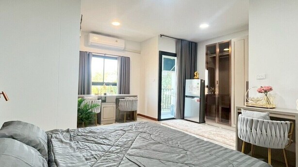 A modern bedroom with a large bed, a desk, and a sliding glass door leading to a balcony. - ✈️ How to Get from Don Mueang Airport to The Rise 789 (Tambon Lak Hok)