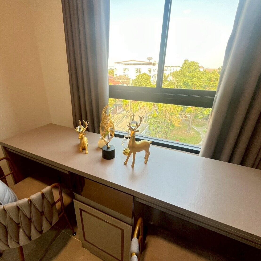 Een bureau met twee hertenbeeldjes en een decoratief object, een stoel, en een uitzicht op gebouwen en bomen door een raam.