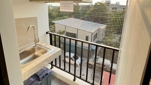 A small balcony with a metal railing, a sink, and a window overlooking a parking area. - ✈️ How to Get from Don Mueang Airport to The Rise 789 (Tambon Lak Hok)