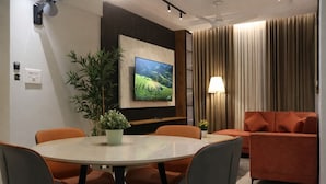 Un salon moderne avec une table de salle à manger ronde, des chaises orange, un canapé, un téléviseur, une plante et une lampe.