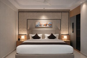 Une chambre d’hôtel moderne avec un grand lit, deux tables de chevet, un ventilateur de plafond et un tableau au-dessus du lit.