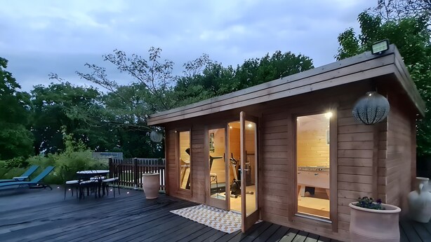 A wooden cabin with a deck, a dining area, and exercise equipment visible through the windows.