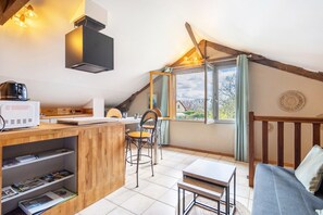 Une cuisine chaleureuse avec un comptoir en bois, un coin repas avec une table et des chaises, un canapé et une grande fenêtre avec des rideaux.