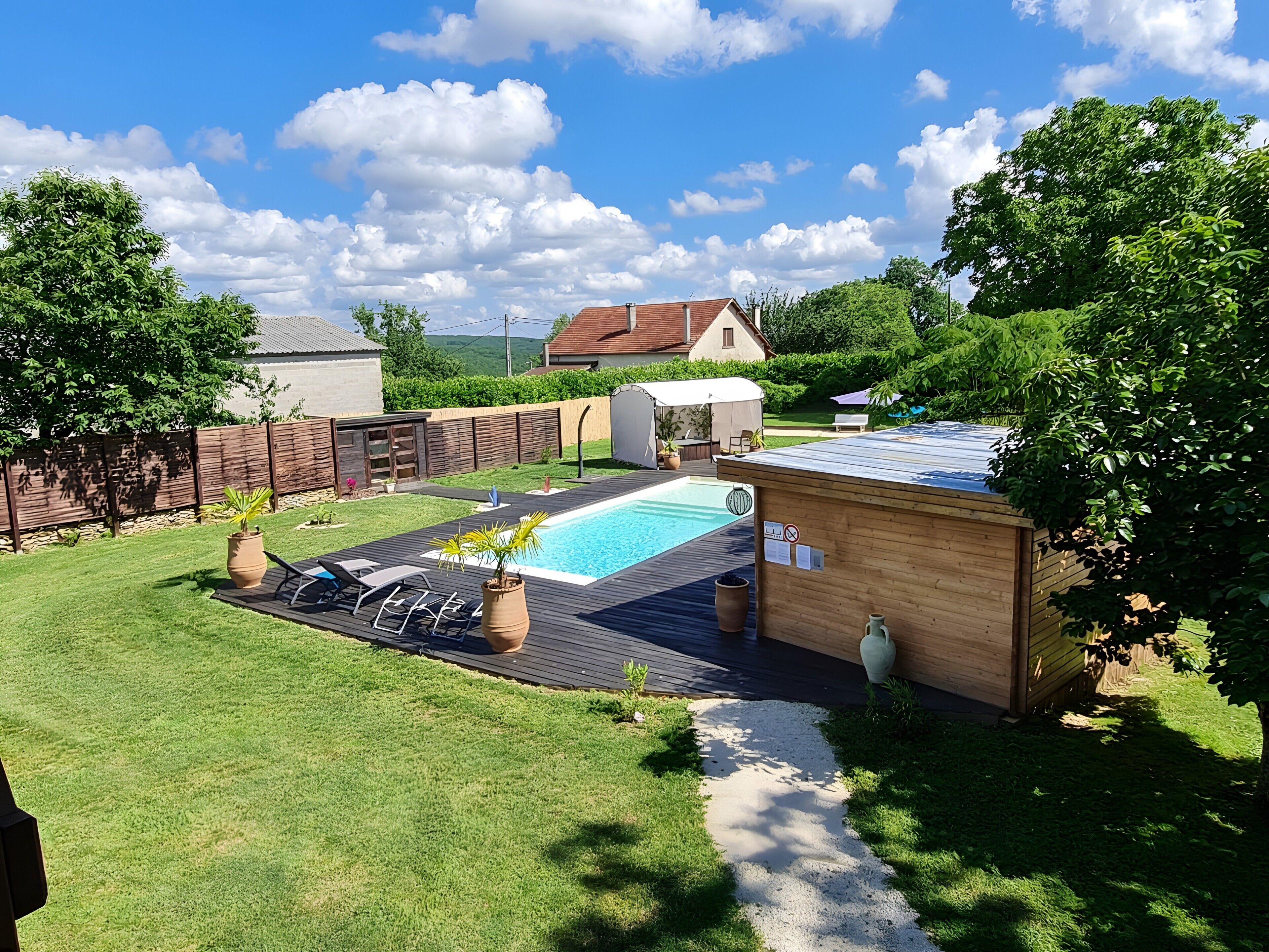 Un patio trasero con piscina, una terraza de madera y un cobertizo pequeño.