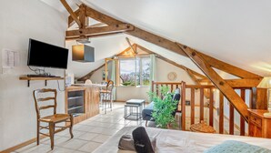 A cozy attic room with a bed, a TV, wooden beams, a window, and a small dining area.