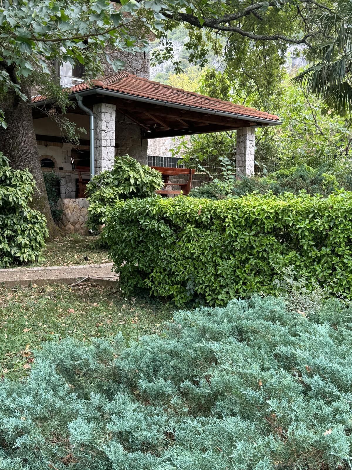 Ein Gebäude aus Stein mit Ziegeldach, umgeben von üppiger Vegetation und einem gepflegten Garten.