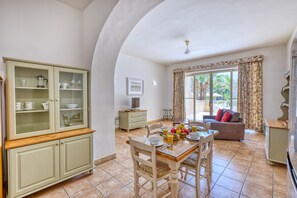 A dining area with a table set for breakfast, a cabinet with glass doors, and a sofa in the background. - Ta Frenc Apartments - 1 BDR, 1 BTH (L-Għasri)