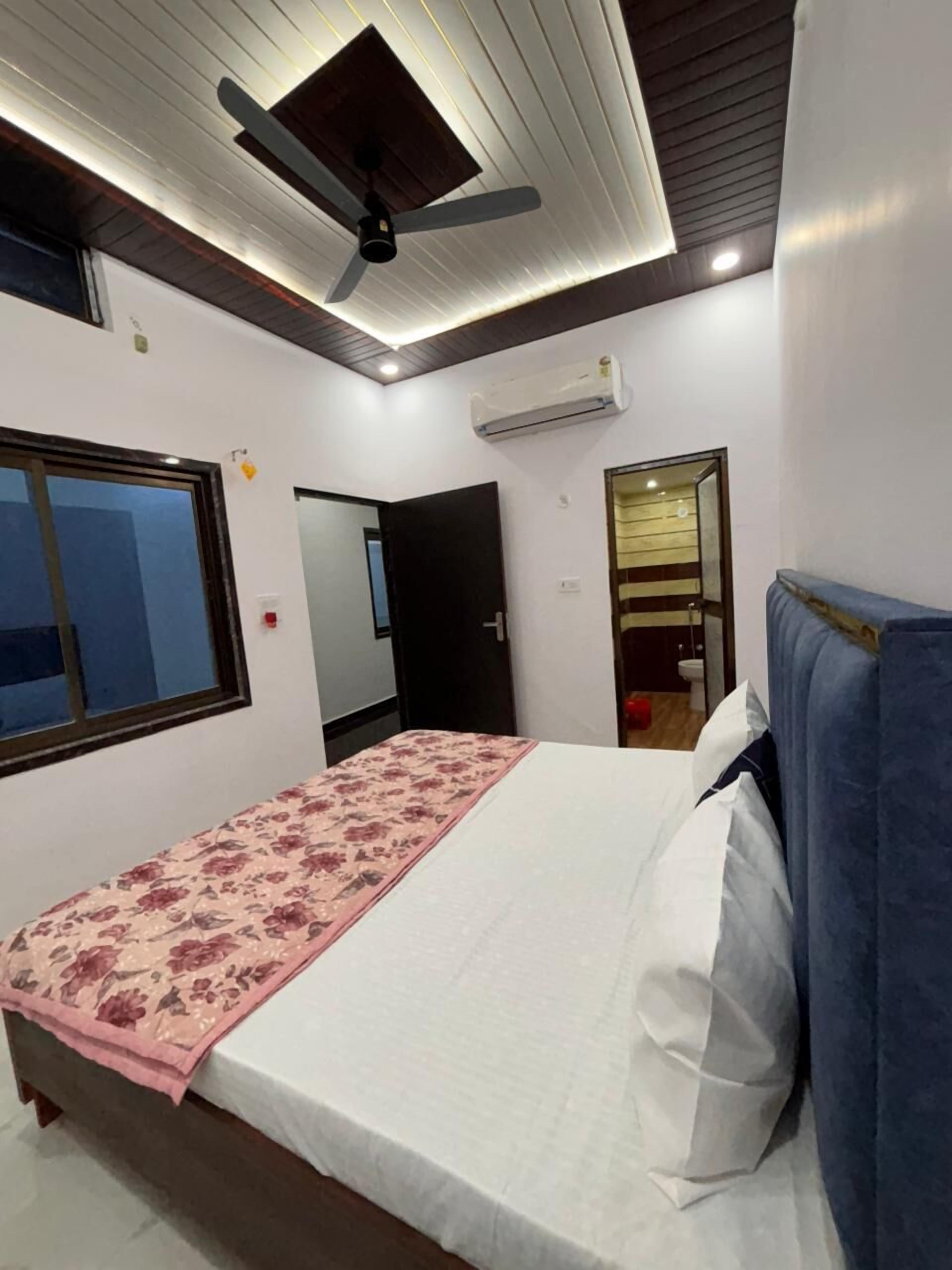 A bedroom with a bed, a ceiling fan, an air conditioning unit, a window, and a door.