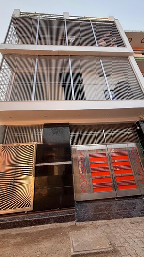 Een meerlaags gebouw met een metalen hekwerk op de bovenste verdieping, een zwart luifel en een rode decoratieve plaat op de begane grond.