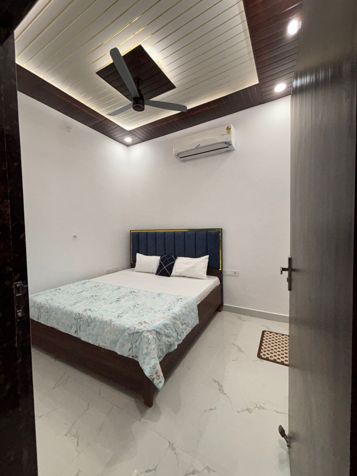 Ein Schlafzimmer mit einem Bett, einem Deckenventilator, einer Klimaanlage und einer Tür.