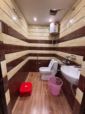 Een kleine badkamer met toilet, wastafel, douche en een rode kruk.