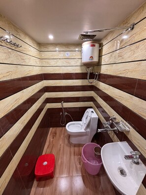 Un bagno con il water, un bidet, un lavandino e uno sgabello rosso.