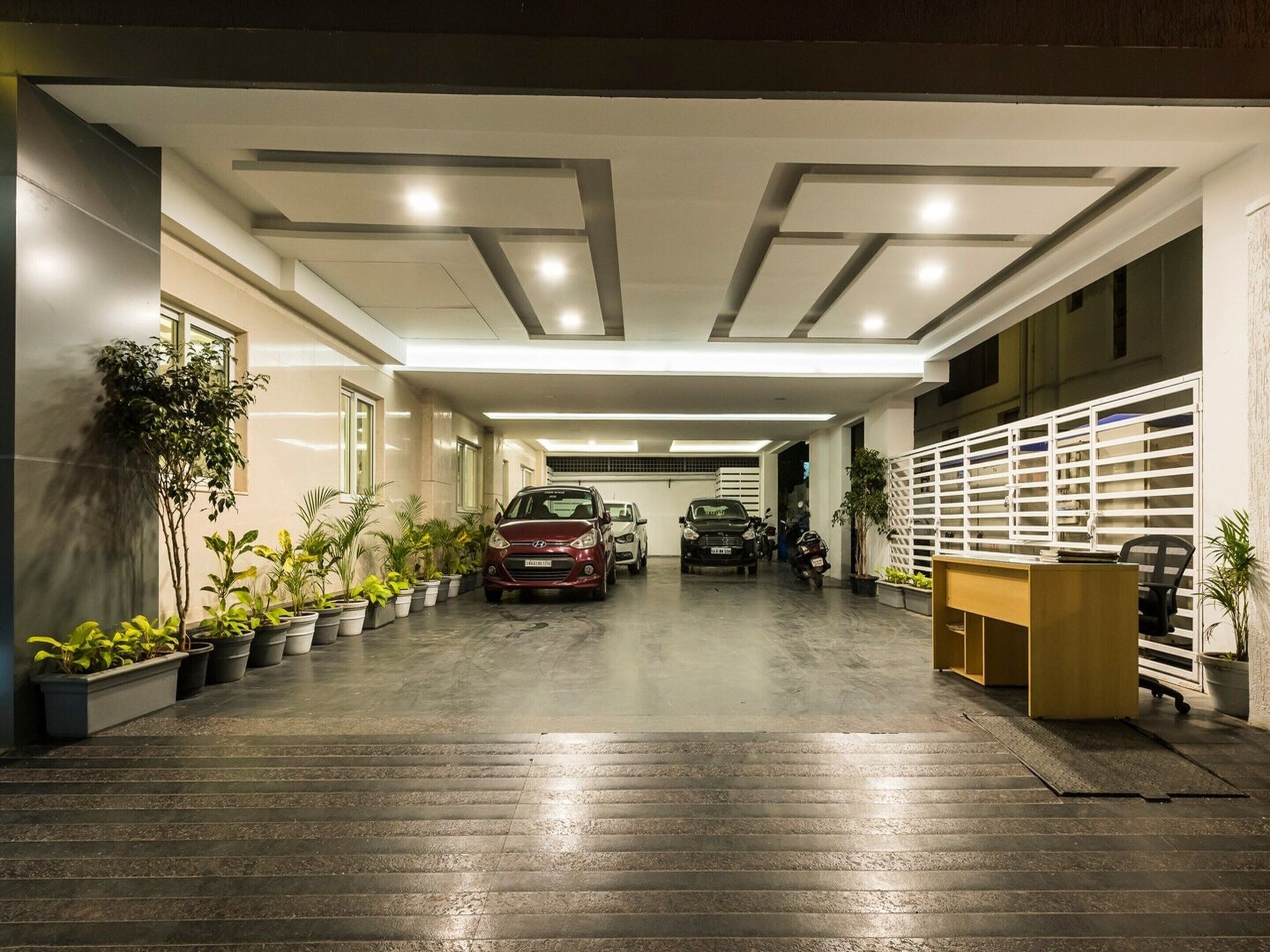 Un parking intérieur moderne, avec une voiture et une moto, des plantes en pot et un comptoir d’accueil.