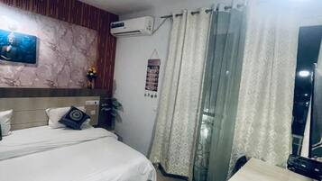 Habitación de hotel con cama, escritorio, ventilador de techo, aire acondicionado y ventana con cortinas.
