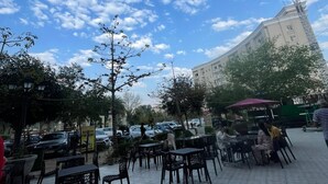 An outdoor cafe area with tables and chairs, a clear sky, and a building in the background. - Brij Darshan (Vrindavan)