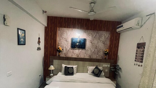 A bedroom with a bed, a ceiling fan, an air conditioning unit, and a small rug. - Brij Darshan (Vrindavan)