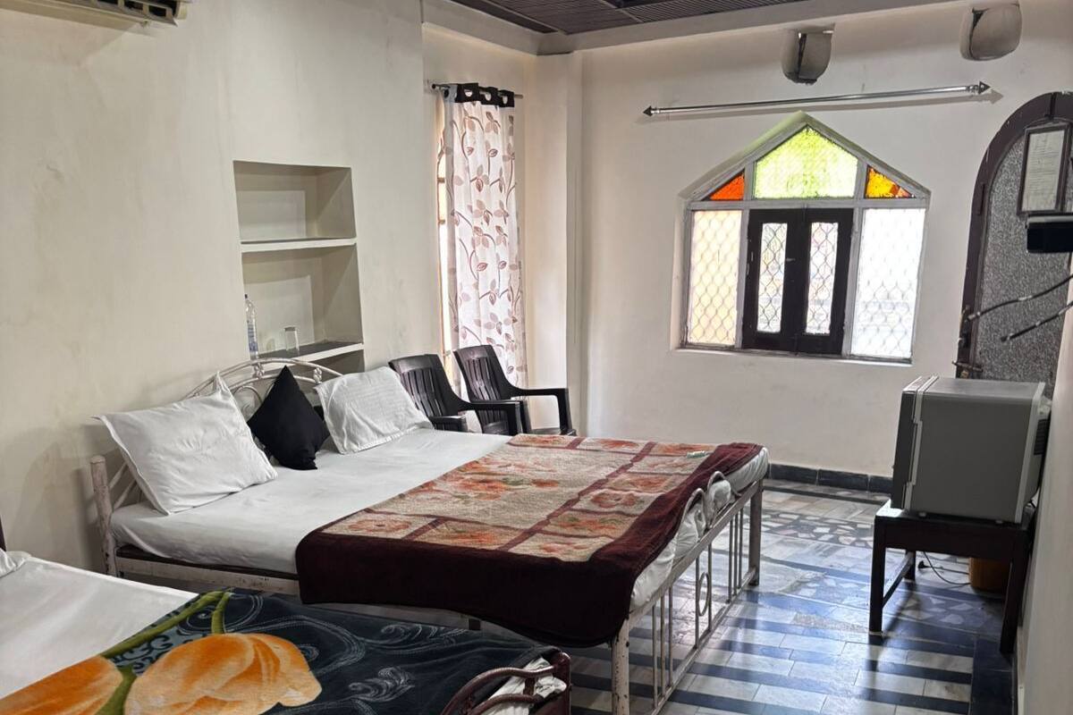 Une chambre d’hôtel avec deux lits, une petite table, une chaise, une fenêtre donnant sur un beau paysage et un ventilateur de plafond.