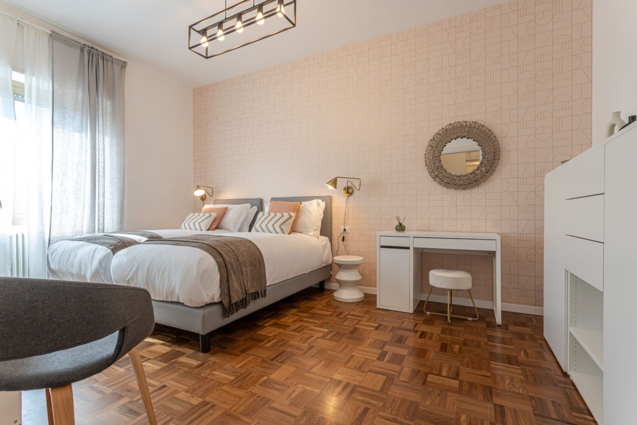 A modern bedroom with a bed, bedside tables, a desk, and a chair.