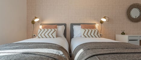 Una cama doble con dos mesitas de noche, cada una con una lámpara, en una habitación con papel tapiz estampado y un espejo en la pared.