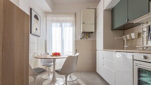 A modern kitchen with white cabinets, a built-in oven, and a dining area with a round table and two chairs. - LUMINOSO APPARTAMENTO AL PIGNETO (ROMA)