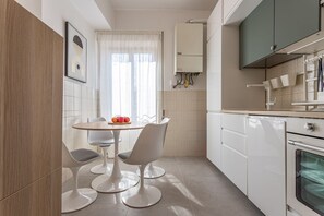 A modern kitchen with white cabinets, a built-in oven, and a dining area with a round table and two chairs. - LUMINOSO APPARTAMENTO AL PIGNETO (ROMA)