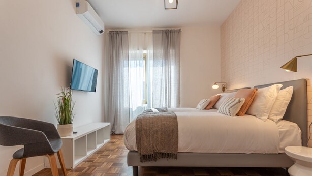 A modern bedroom with a bed, a TV, a plant, and a bench. - LUMINOSO APPARTAMENTO AL PIGNETO (ROMA)