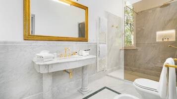 A bathroom with a marble sink, a large mirror, a toilet, and a shower area.
