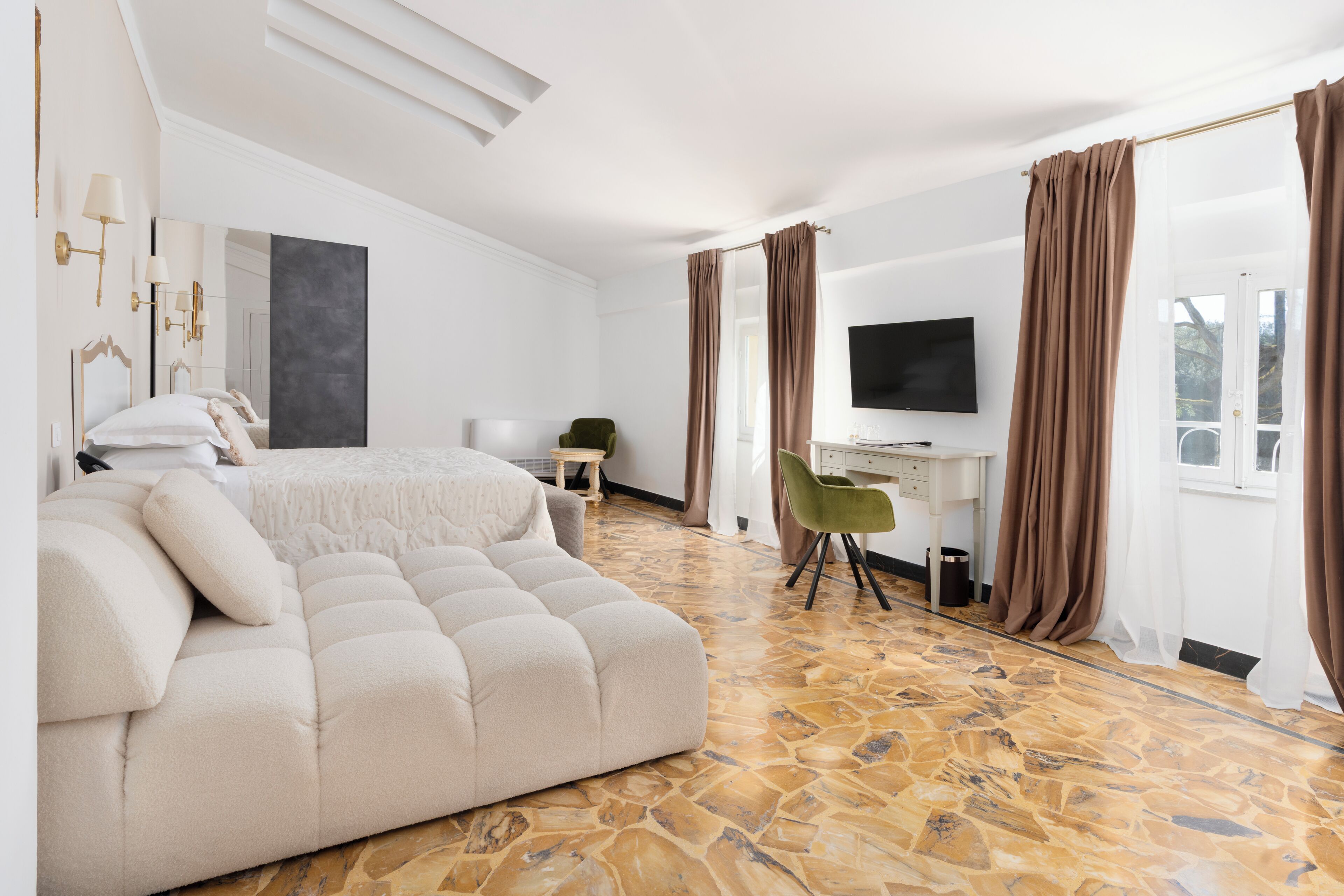 A modern bedroom with a large bed, a desk, a television, and a stone-patterned floor.