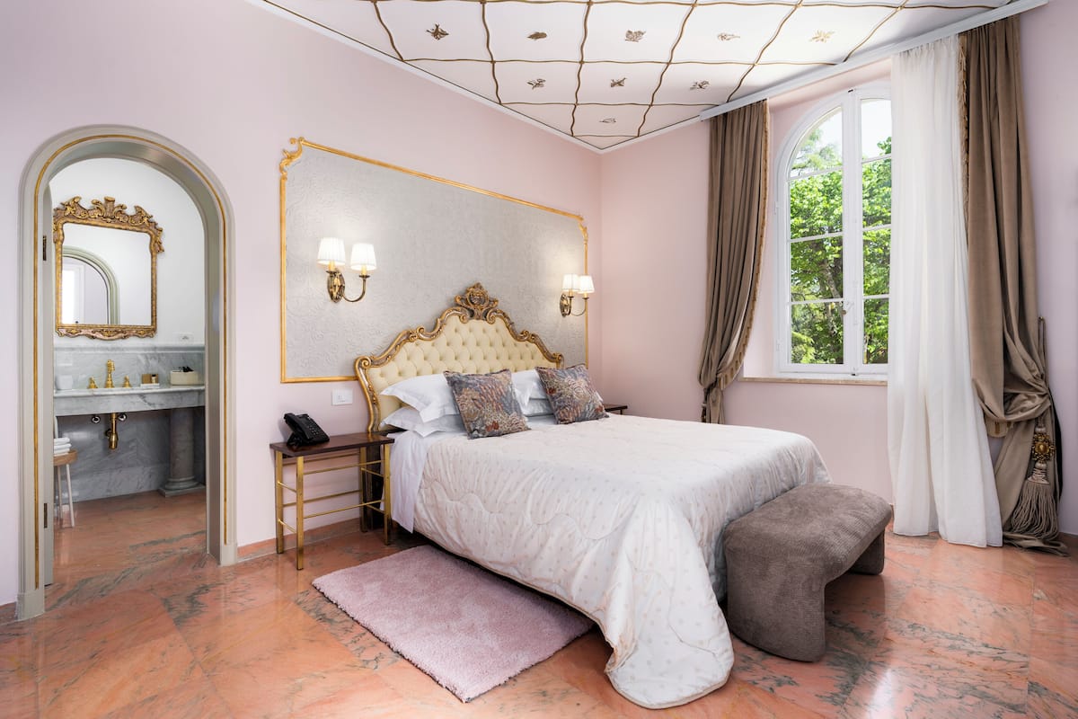 Ein Schlafzimmer mit einem großen Bett, einem Schminktisch mit Spiegel und einem Fenster mit Vorhängen.