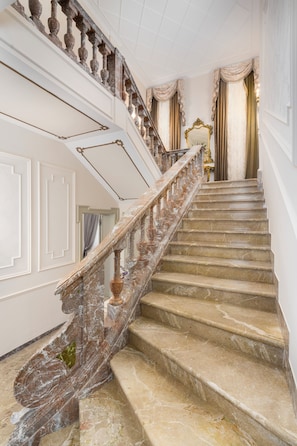 Una imponente escalera de mármol con barandillas ornamentadas, que conduce a un cuarto con un espejo grande y cortinas.
