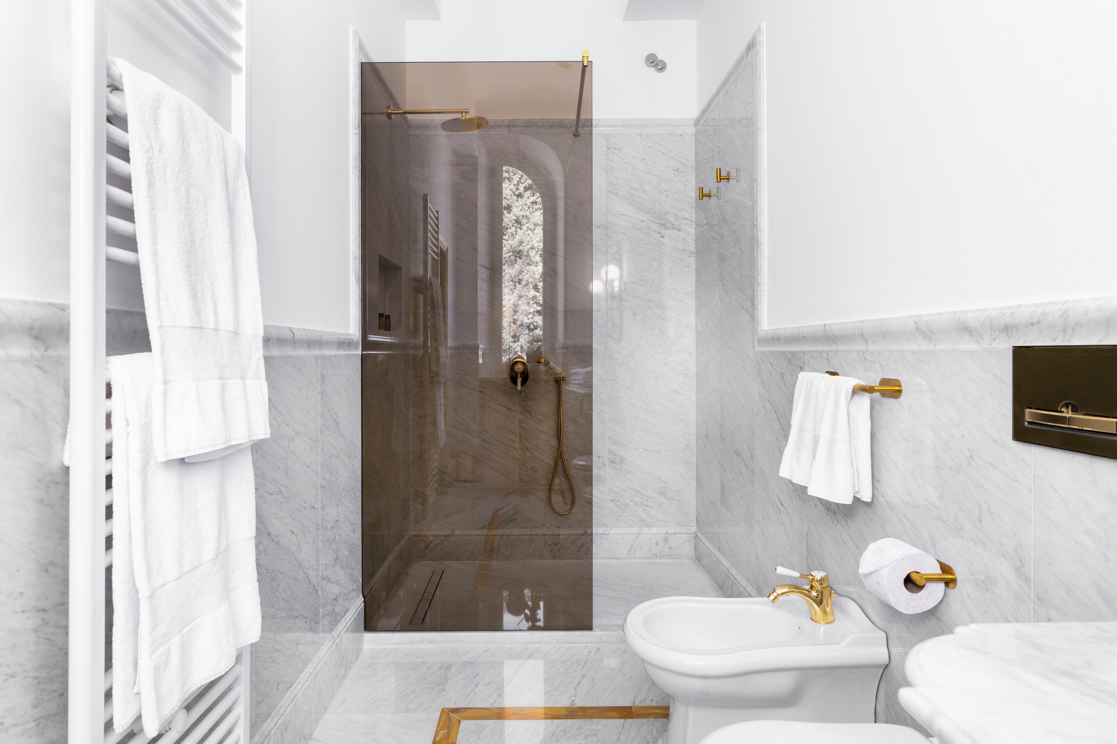 Une salle de bain moderne avec une douche en verre, des murs en marbre et un lavabo blanc agrémenté de robinetterie dorée.