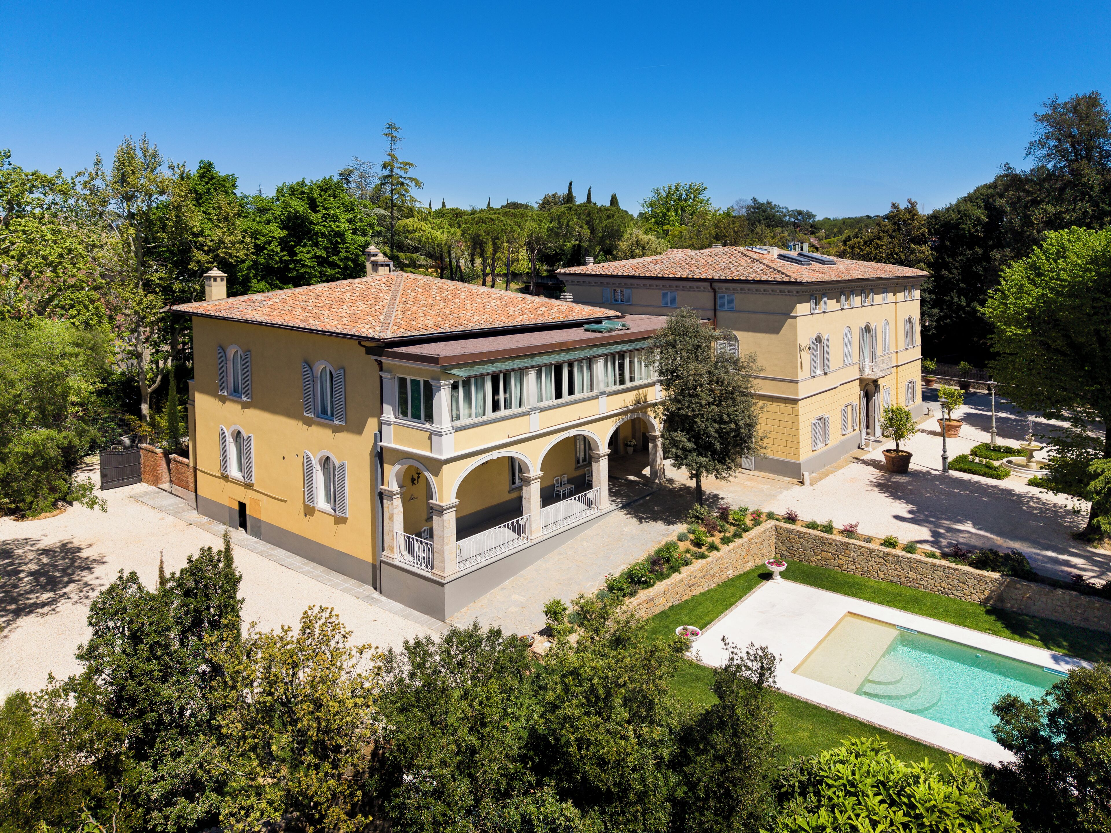 A two-story villa with a swimming pool, surrounded by lush greenery and trees.