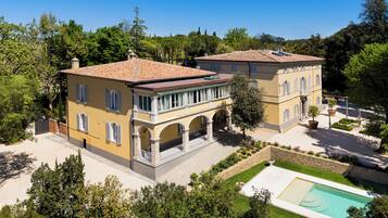 A two-story villa with a swimming pool, surrounded by lush greenery and trees.