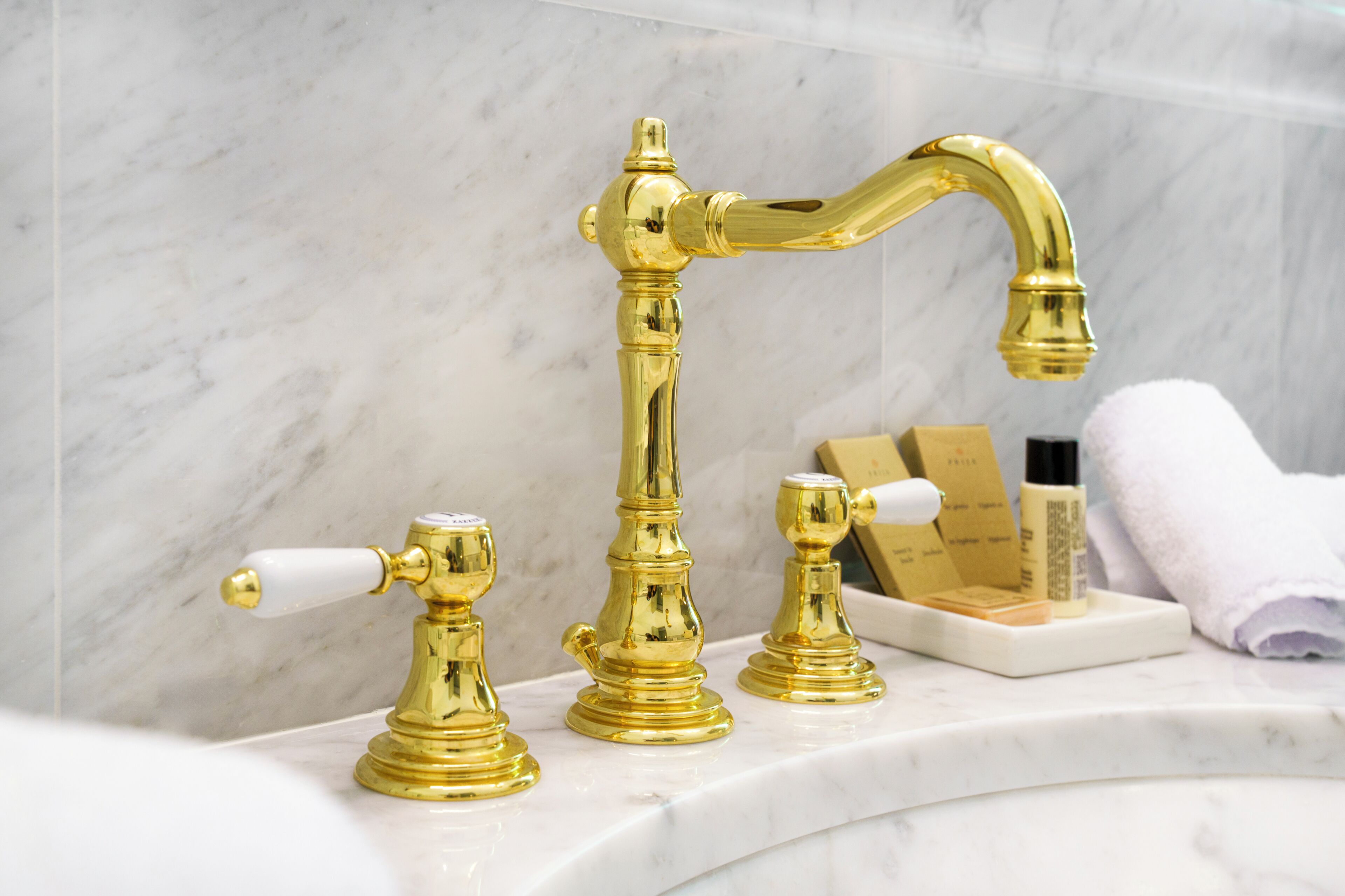 Un bagno con rubinetto dorato, piano di lavoro in marmo e articoli da toilette.