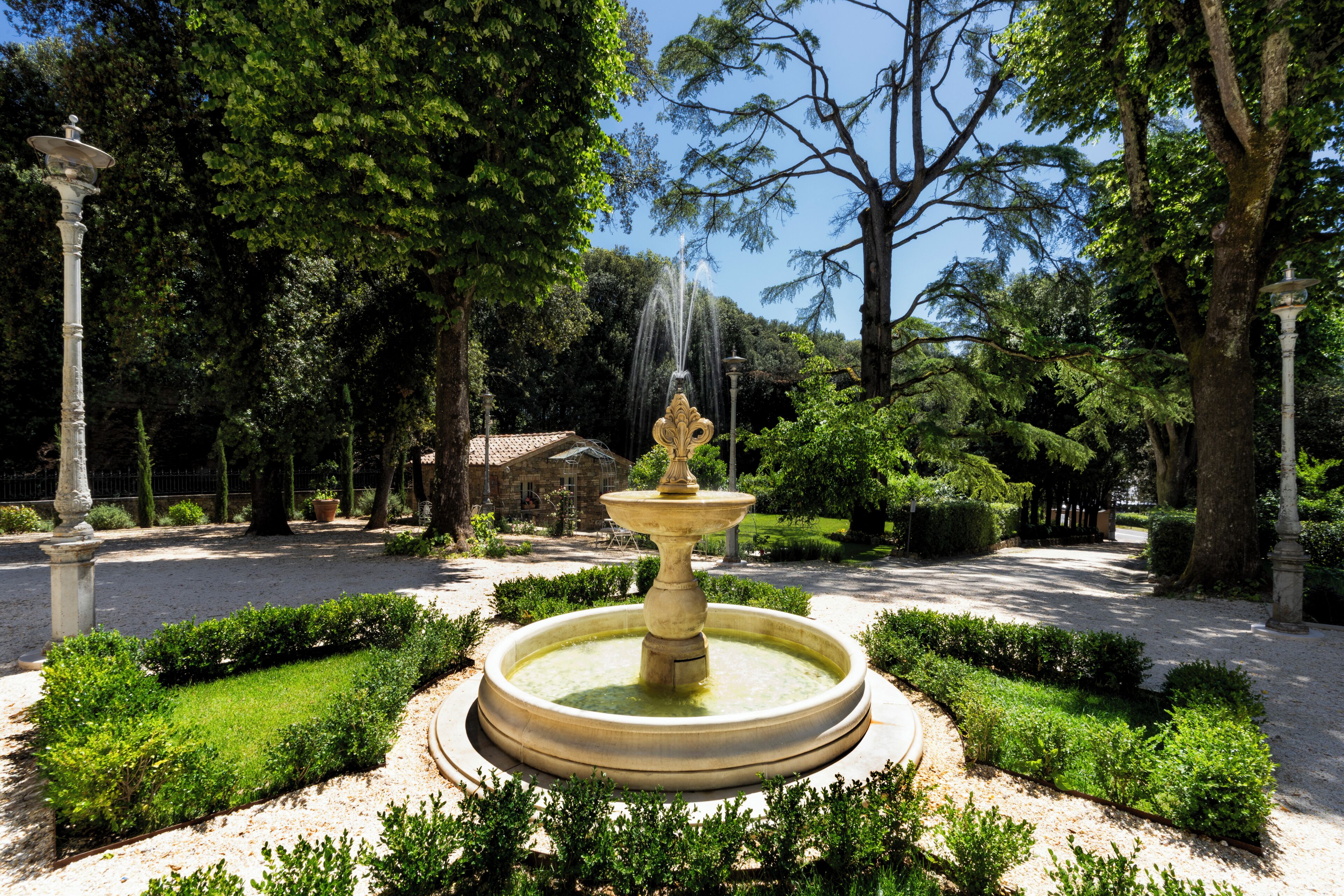 A fountain surrounded by manicured hedges and trees in a park setting.