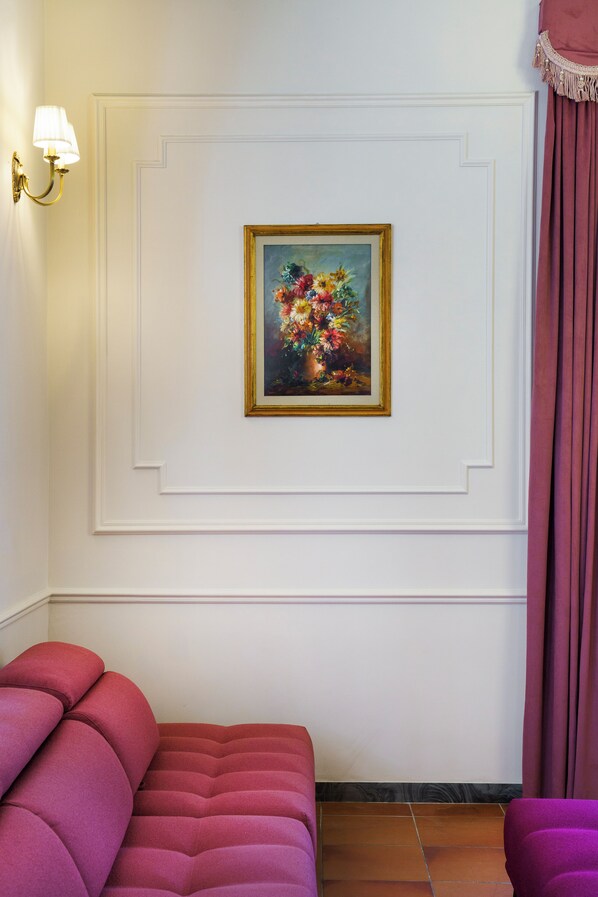 A room with a white wall, a framed painting, a purple sofa, and a wall-mounted light fixture. - Hotel Villa L'Avvenire (Siena)