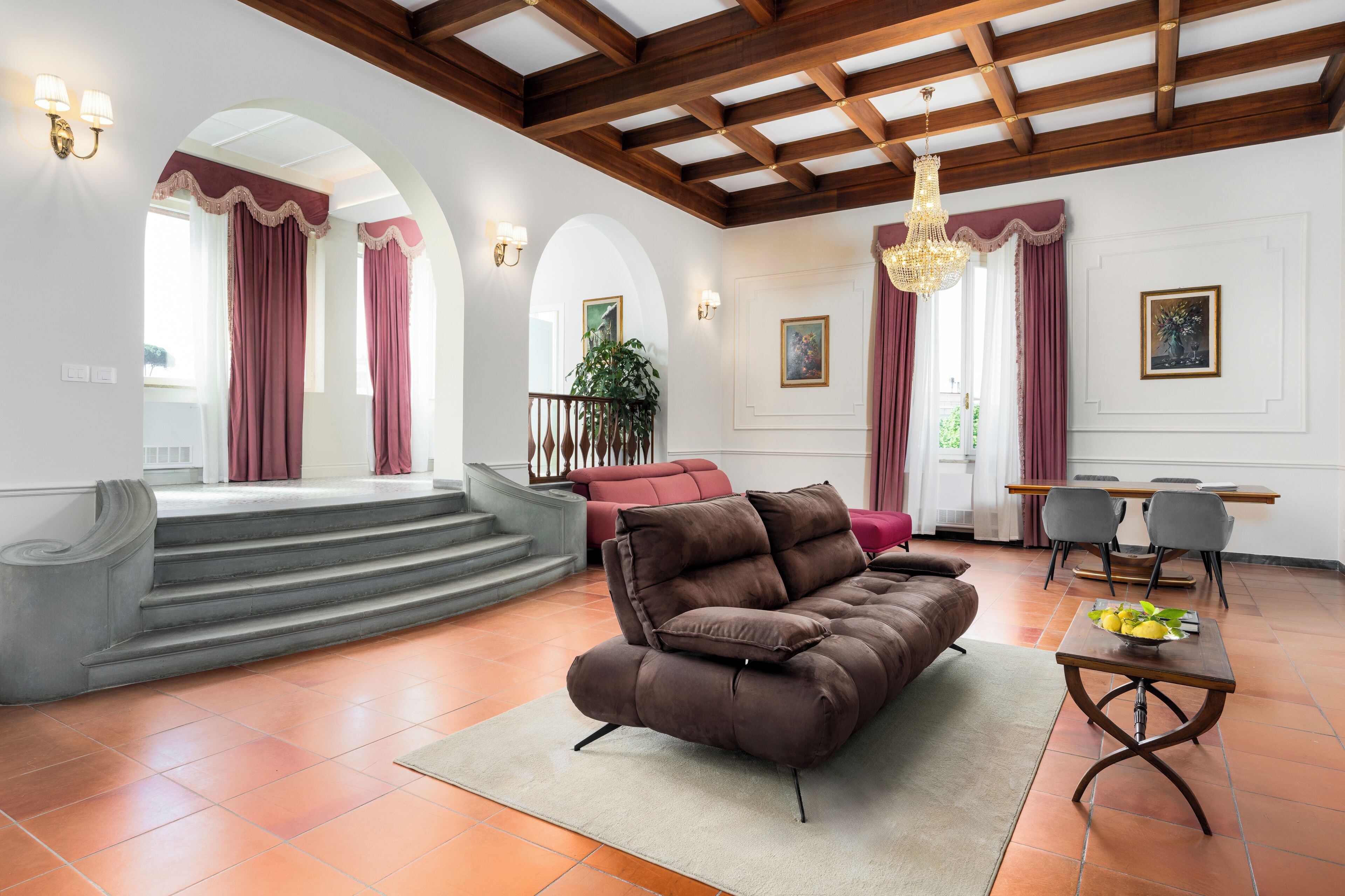 A spacious living area with a brown sofa, a dining table with chairs, and a staircase leading to an upper level.