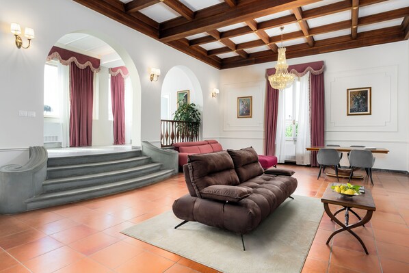 A spacious living area with a brown sofa, a dining table with chairs, and a staircase leading to an upper level. - Hotel Villa L'Avvenire (Siena)