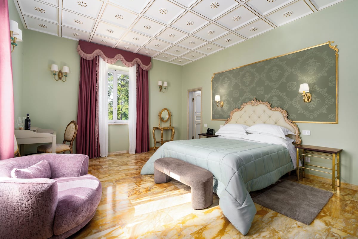 Ein Schlafzimmer mit Bett, einer Bank, einem Sessel, einem Schminktisch und einem großen Spiegel.