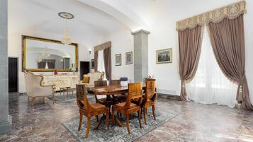 Un comedor con suelo de mármol, una mesa redonda, sillas de madera, una lámpara de araña y un espejo grande.